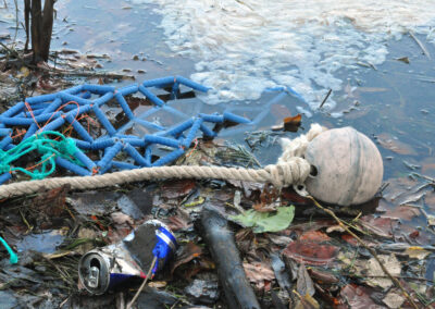 Filet de pêche et bouée sur berge à moitié dans l'eau avec de déchets autour incluant une canette de soda