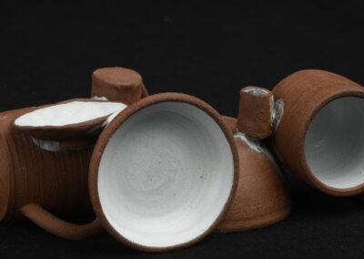 Brique de céramique constituée de mini tasses, assiettes et bols. Argile terra cotta marron foncé et intérieur des pièces en émail blanc.