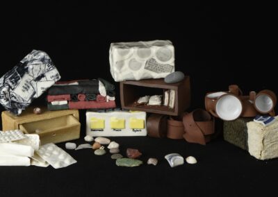 Des briques en céramique ont été réalisé à partir de différents objets comme des médicaments, une ceinture en cuir, des tampons de passeport... Elles sont de différentes couleurs et argiles et empilées en arc de cercle. L'ensemble est photographié sur un fond noir.