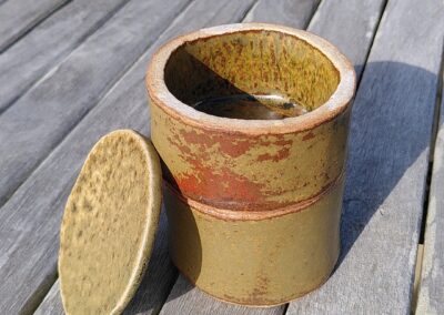 Une double boite en céramique cylindrique avec couvercle sur une table en bois.