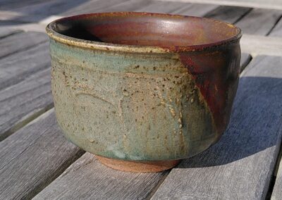 Bol en céramique sur table en bois. Le bol est rouge et vert celadon.